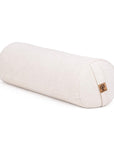 A cylindrical yoga bolster pillow in a natural off-white linen fabric, featuring a small cork patch on one end, set against a plain white background